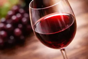 Bicchiere di vino rosso con uva, su sfondo di legno. Eleganza e gusto.