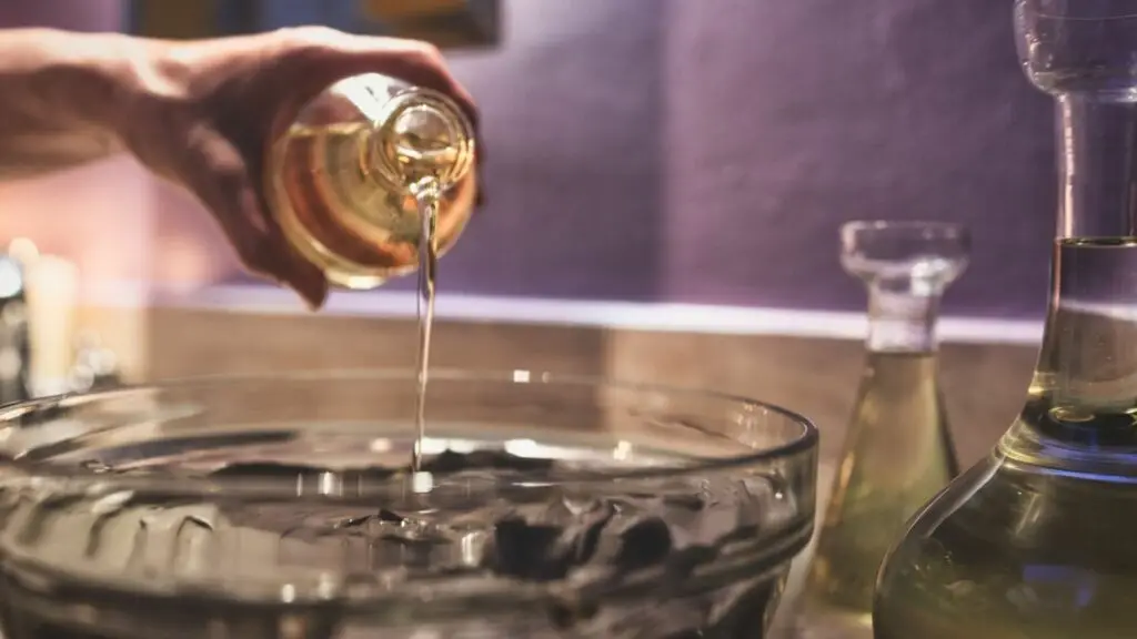 Mano che versa olio in una ciotola di vetro. Cura del corpo, idratazione.