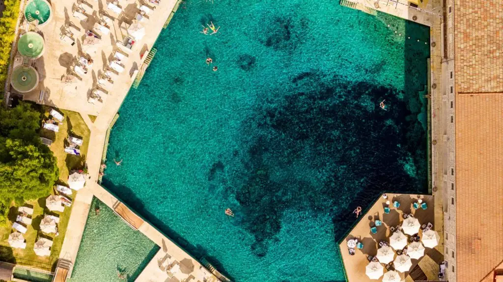 Vista aerea della piscina termale di Saturnia con persone che nuotano e prendono il sole.