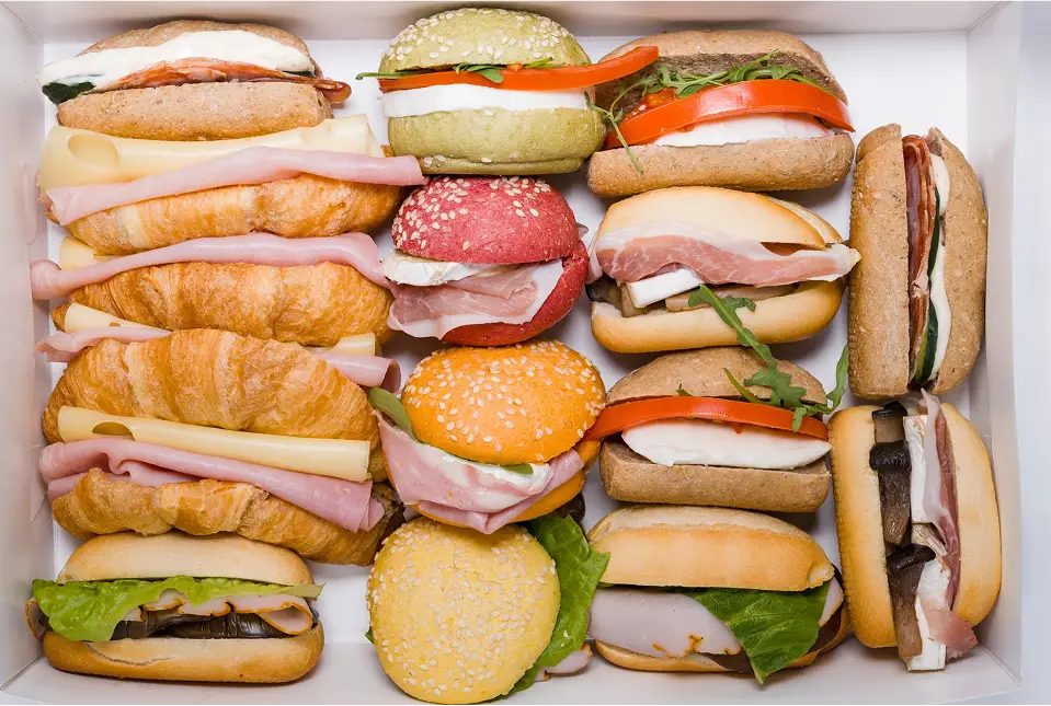 Assortimento di panini gourmet colorati in scatola. Panini con prosciutto, formaggio e verdure fresche.