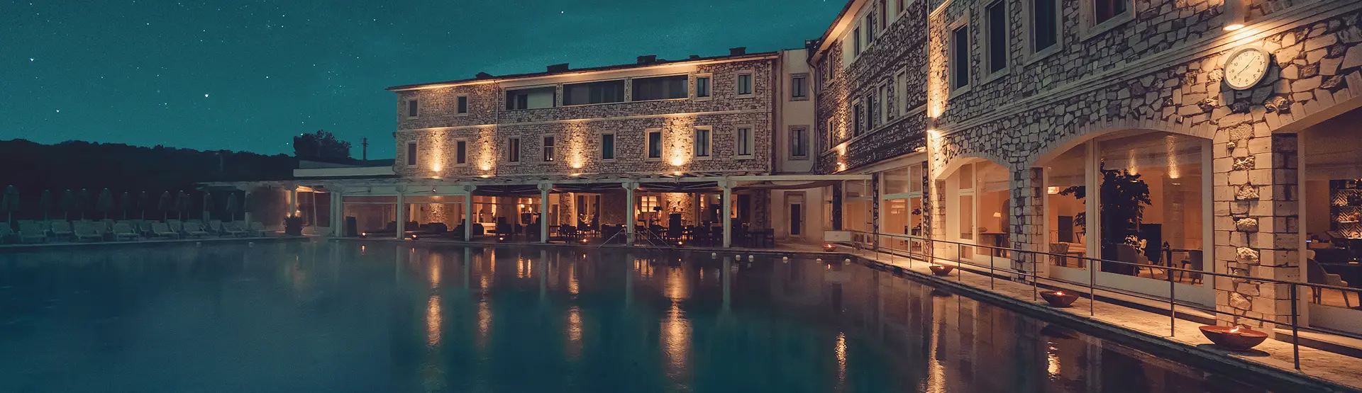 Club notturno illuminato riflesso in piscina. Architettura in pietra, luci calde e atmosfera rilassante.