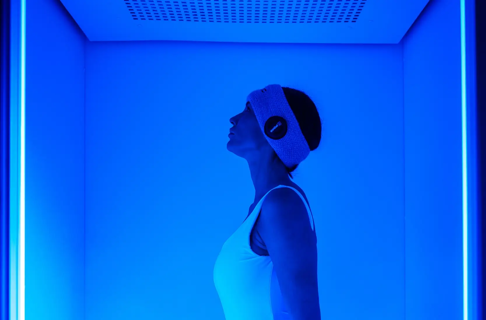 Donna in cabina di crioterapia con luce blu e fascia per la testa. Trattamento di benessere.