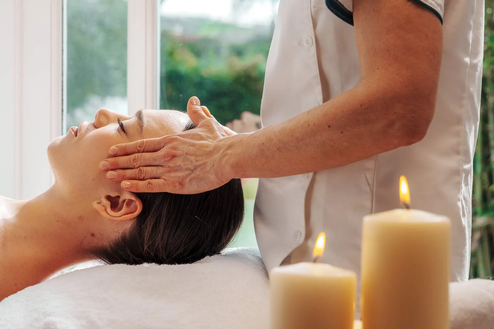 Donna che riceve massaggio al viso, candele accese. Trattamenti benessere.