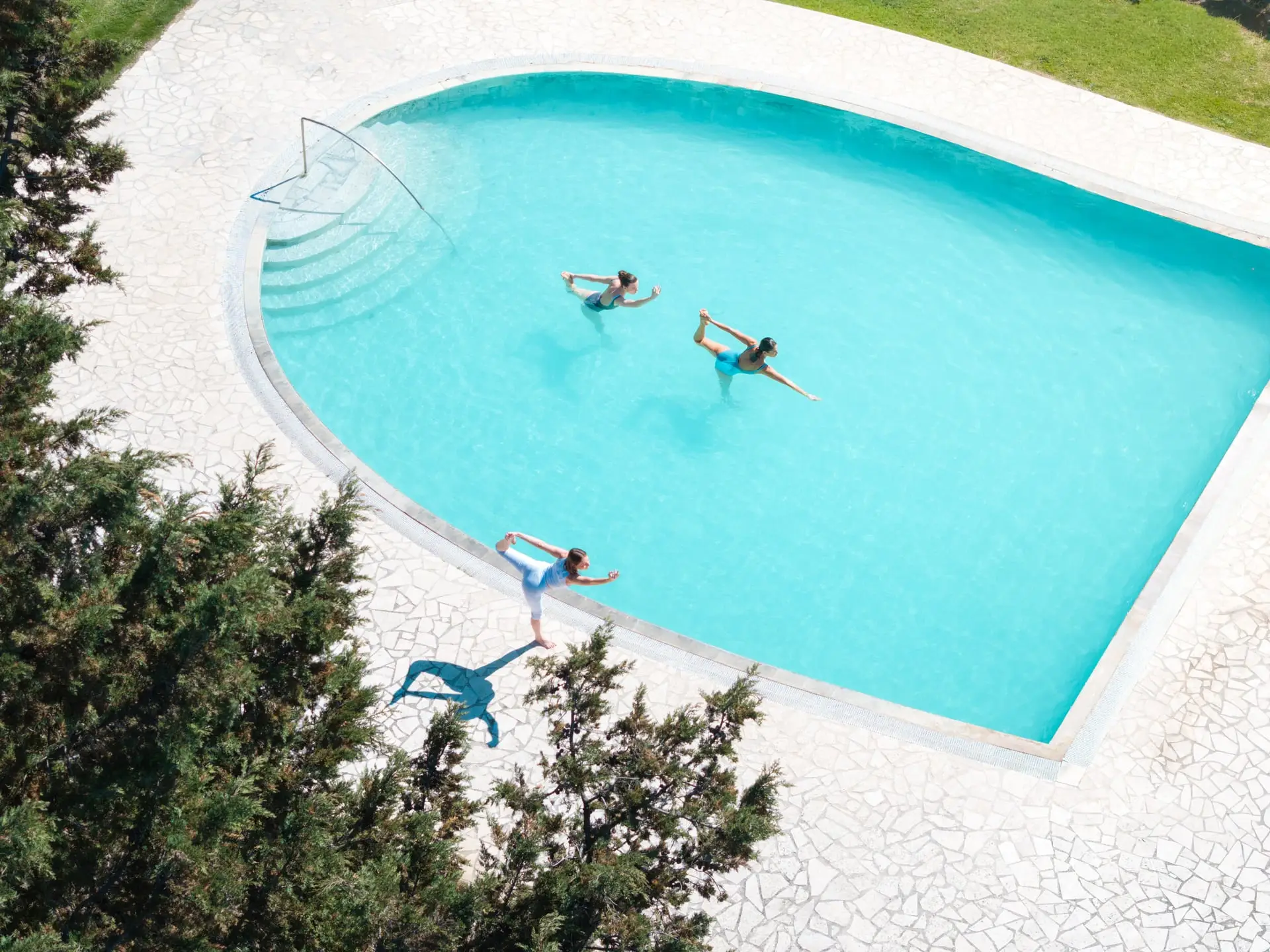 Tre persone che fanno yoga in piscina e a bordo piscina in un club.