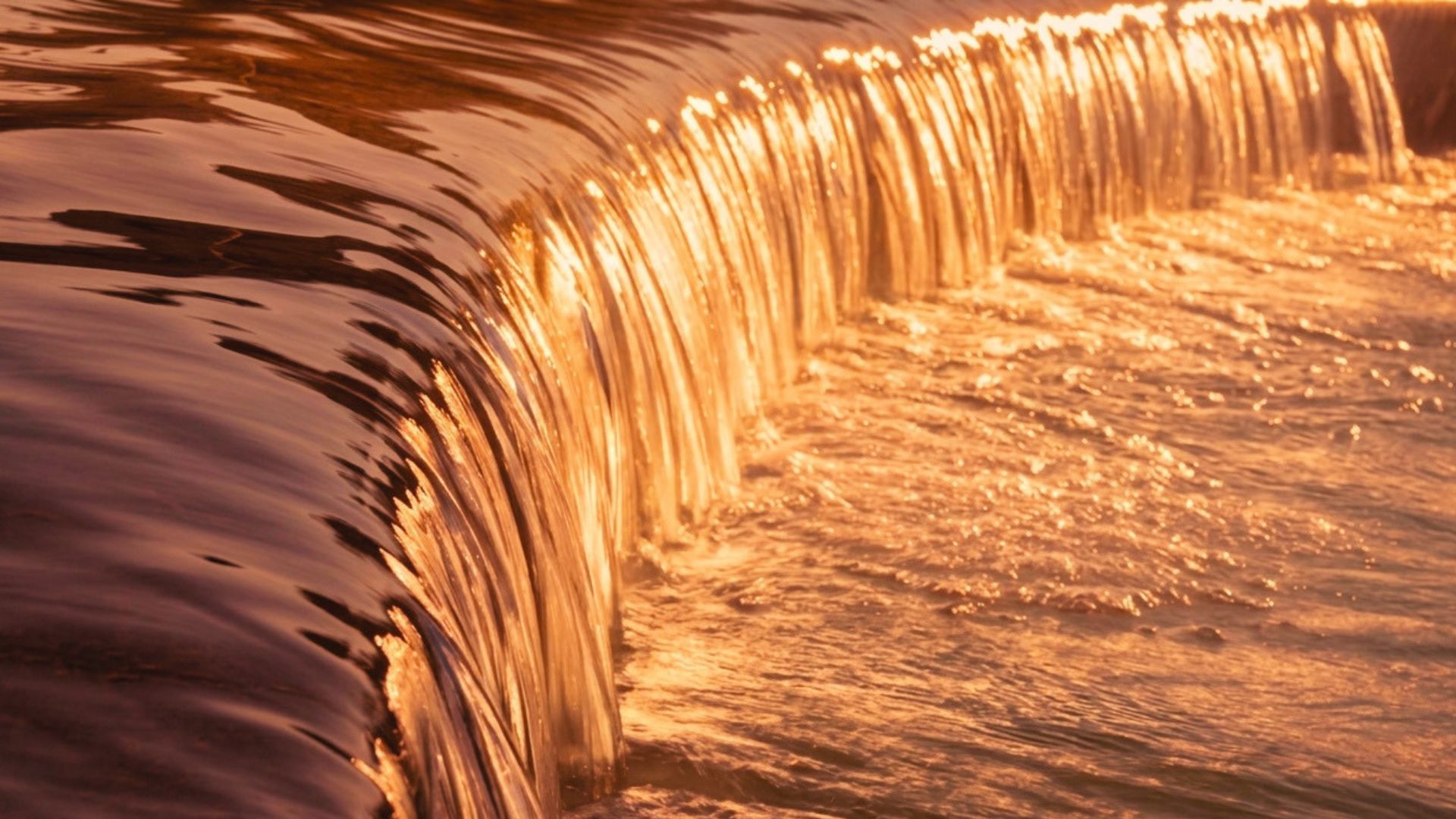 Cascata dorata al tramonto con riflessi caldi sull'acqua.